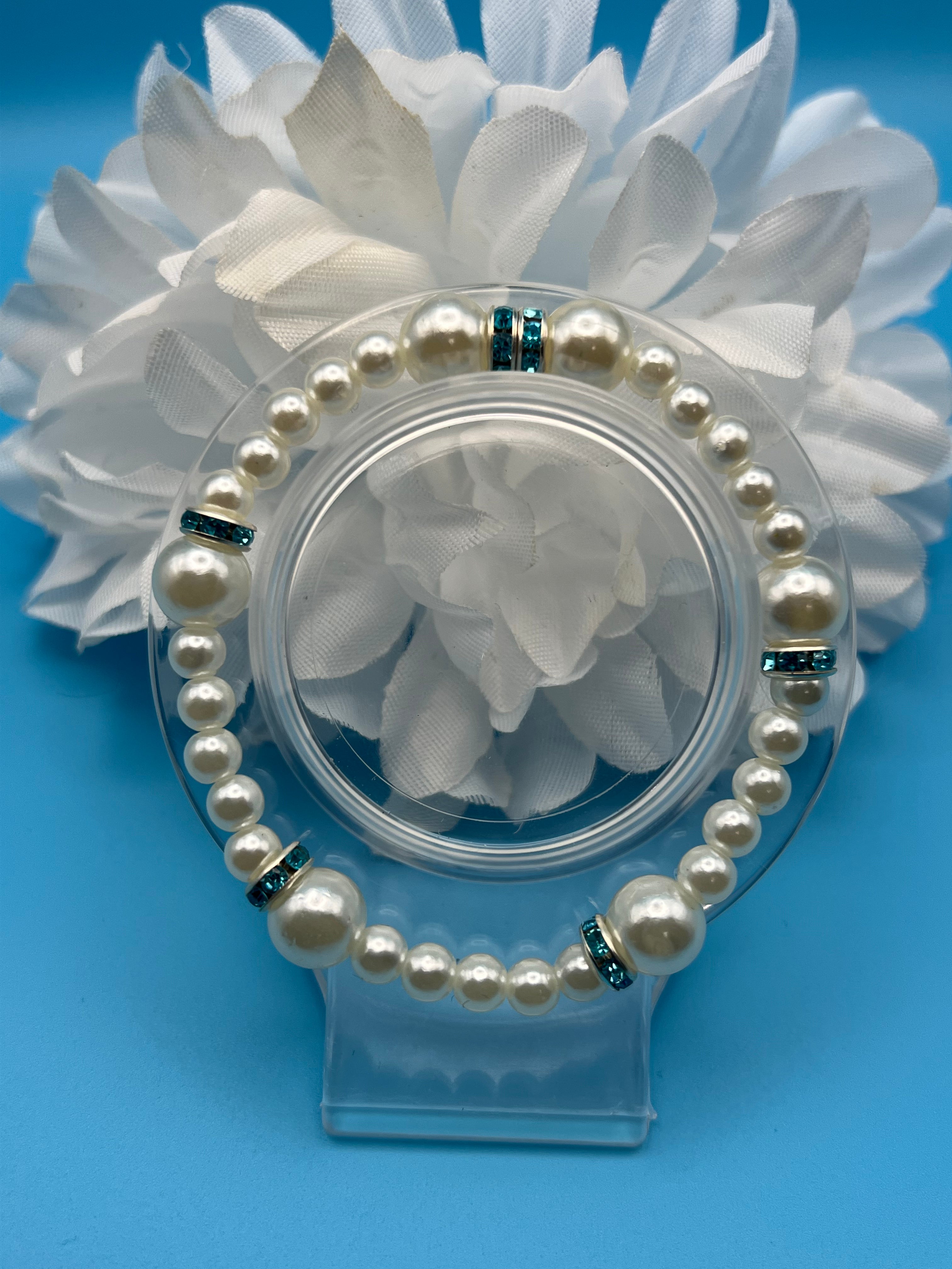 Pearl bracelet in a clear container with white flowers on a blue background